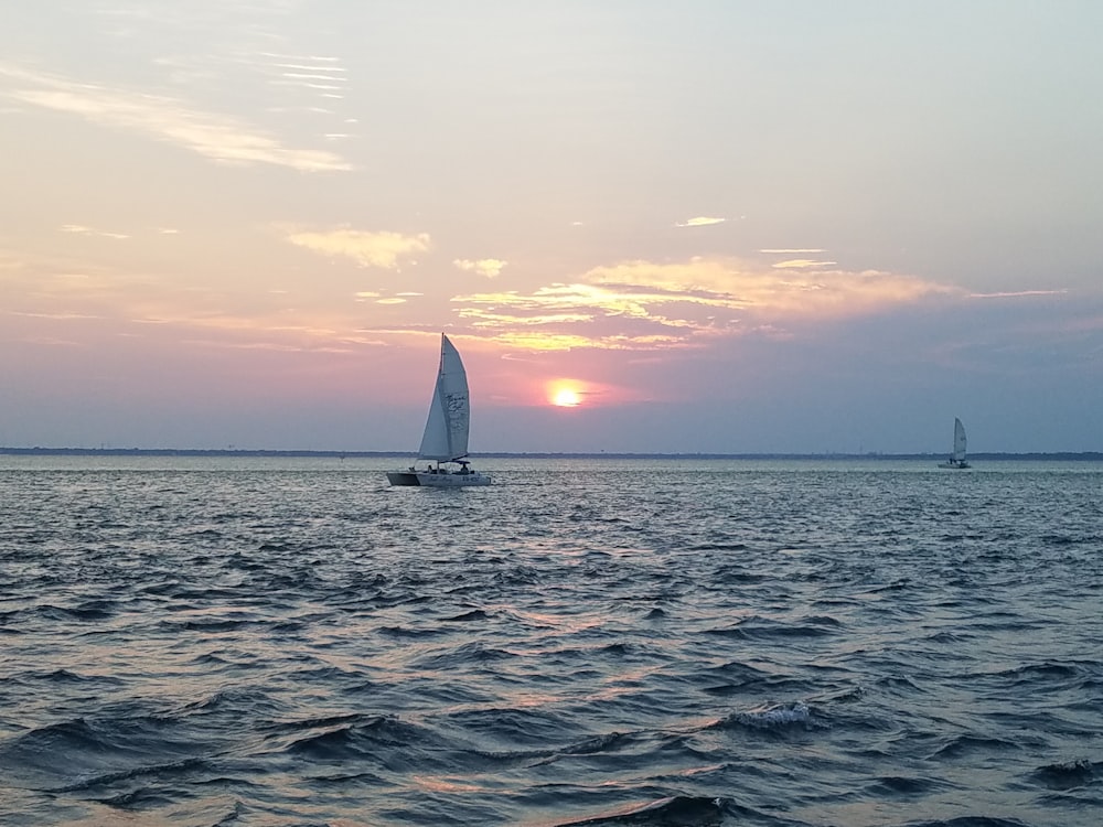 a sailboat in the ocean with a sunset in the background