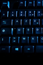 A close-up view of a computer keyboard, featuring black keys illuminated with a blue light. The layout includes numbers, letters, and function keys, with visible labels like Ctrl and Alt keys.