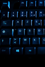 A close-up view of a computer keyboard, featuring black keys illuminated with a blue light. The layout includes numbers, letters, and function keys, with visible labels like Ctrl and Alt keys.