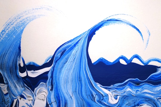 Abstract waves painted in vibrant shades of blue, featuring fluid and swirling brushstrokes that mimic the motion of the ocean. The waves are set against a clean white background, emphasizing the contrast and movement of the painted water.