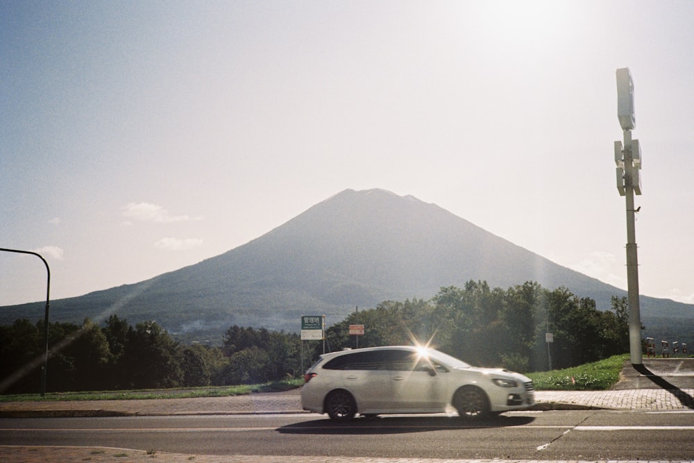 a white car driving down a street next to a tall mountain
