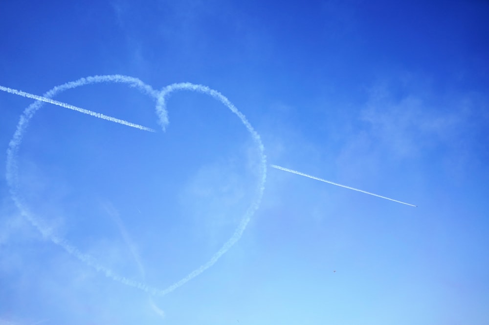 a heart shaped contrail flying through a blue sky