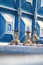 Two metallic valves with wheel handles are attached to horizontal pipes, set against a backdrop of a large blue industrial container. The setting suggests an industrial or mechanical environment with a focus on infrastructure or utilities.