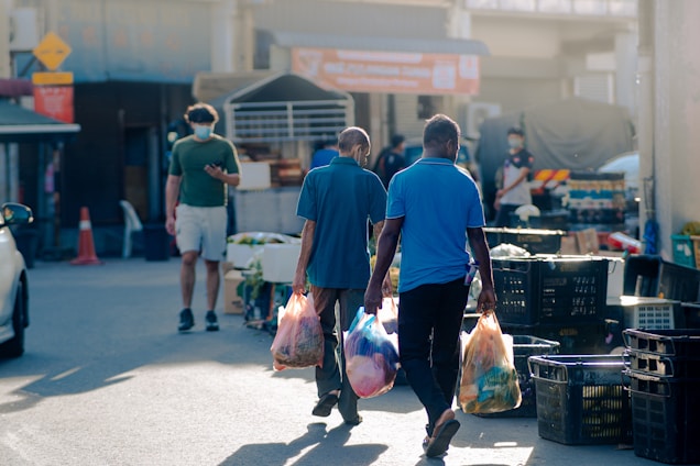 A friendly person carrying grocery bags while walking down a sunny street.