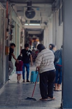 A professional cleaner sweeping the floor in a bright, modern condominium hallway.