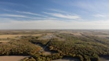 A wide view of green farmland plots with clear roads and trees under a bright sky