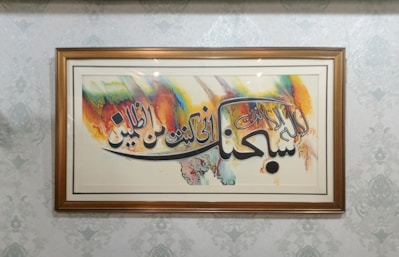 Elegant close-up of a framed Islamic calligraphy piece with gold accents on a minimalist white wall