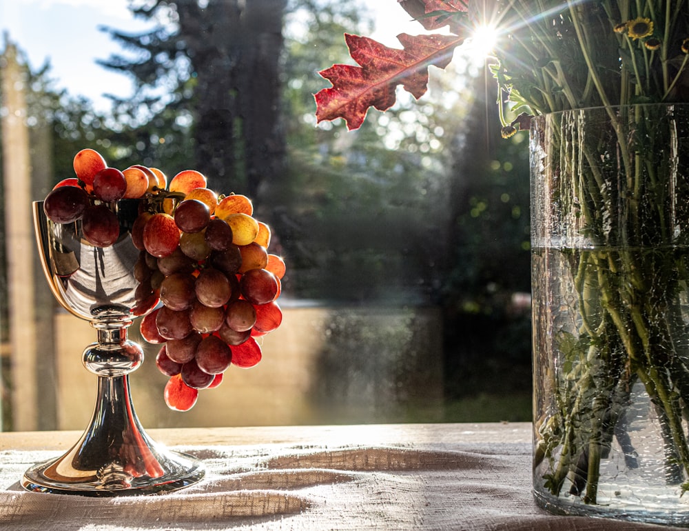 a vase filled with lots of grapes next to a vase filled with flowers