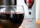 A glass of red wine with reflections of a room featuring windows and furniture, placed in front of a wine bottle with a label that shows a hot air balloon design. The label reads 'Barossa Valley Shiraz, Wine of Australia'.