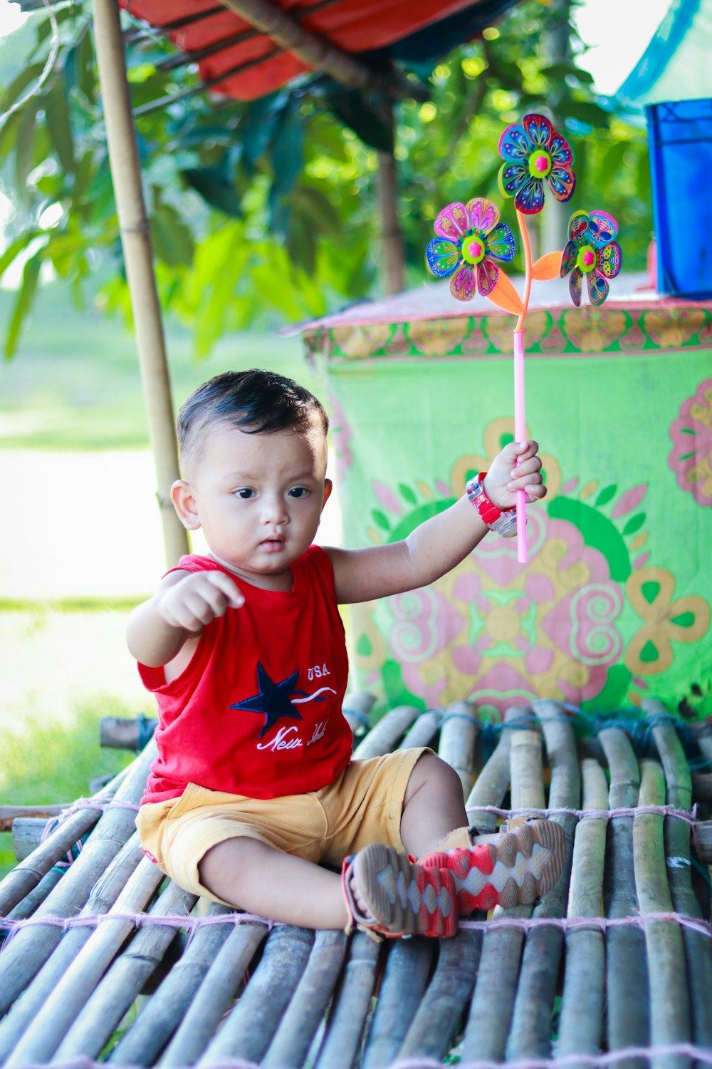 a little boy sitting on a bamboo mat holding a pinwheel