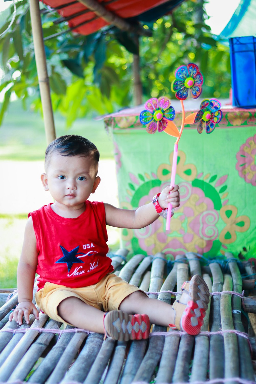 a little boy sitting on a bamboo mat holding a pinwheel