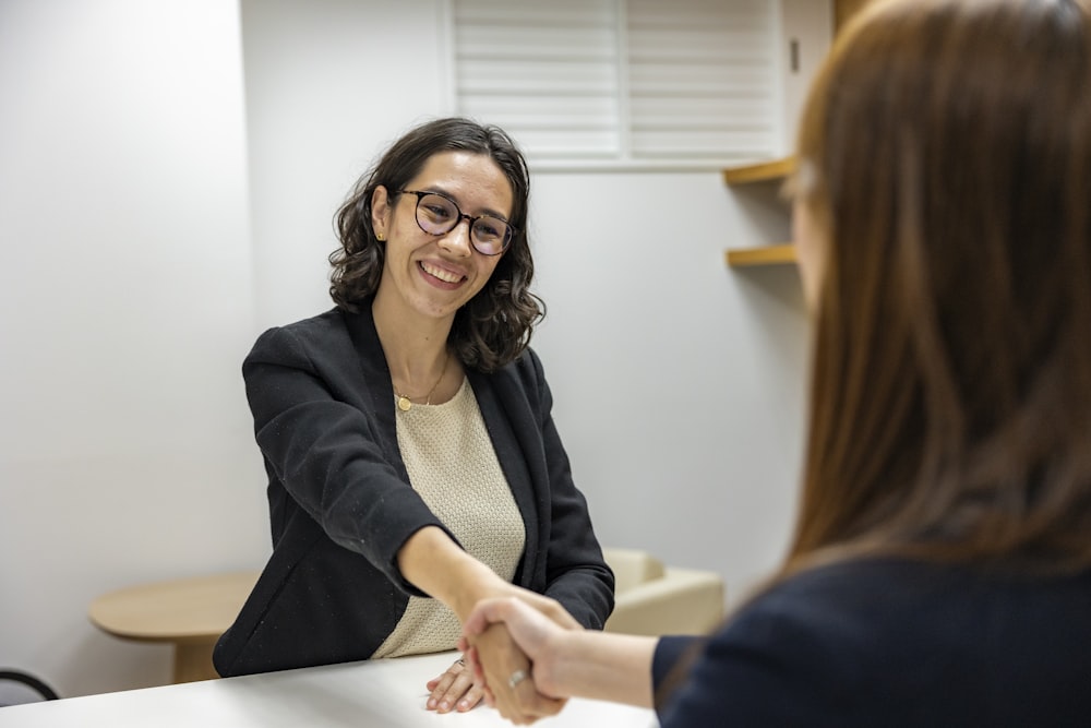 a woman shaking hands with another woman sitting at a table