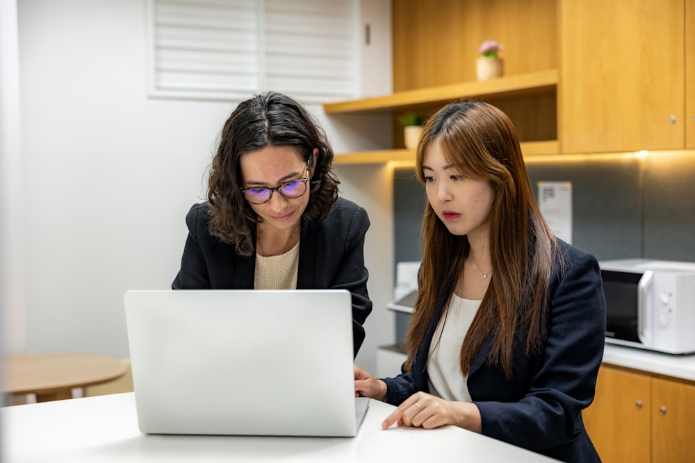 two women sitting at a table looking at a laptop