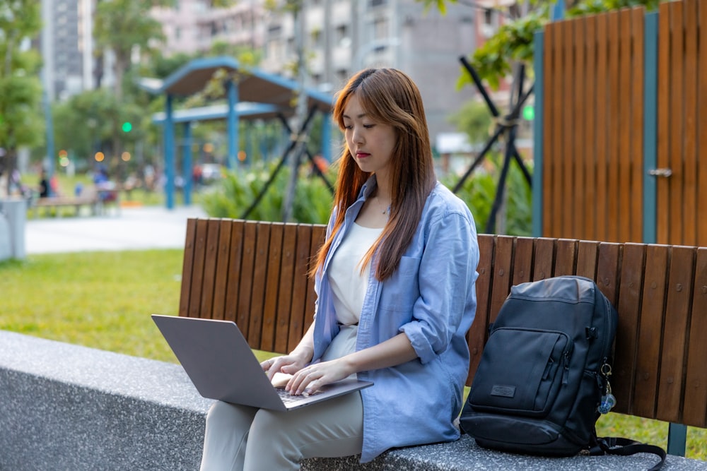a woman sitting on a bench using a laptop computer