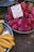 A vibrant market scene with a pile of dragon fruits displayed in a metal bowl, accompanied by a sign in mixed languages referring to the fruit's benefits. Next to the dragon fruits, a separate bowl holds a bunch of ripe yellow bananas.