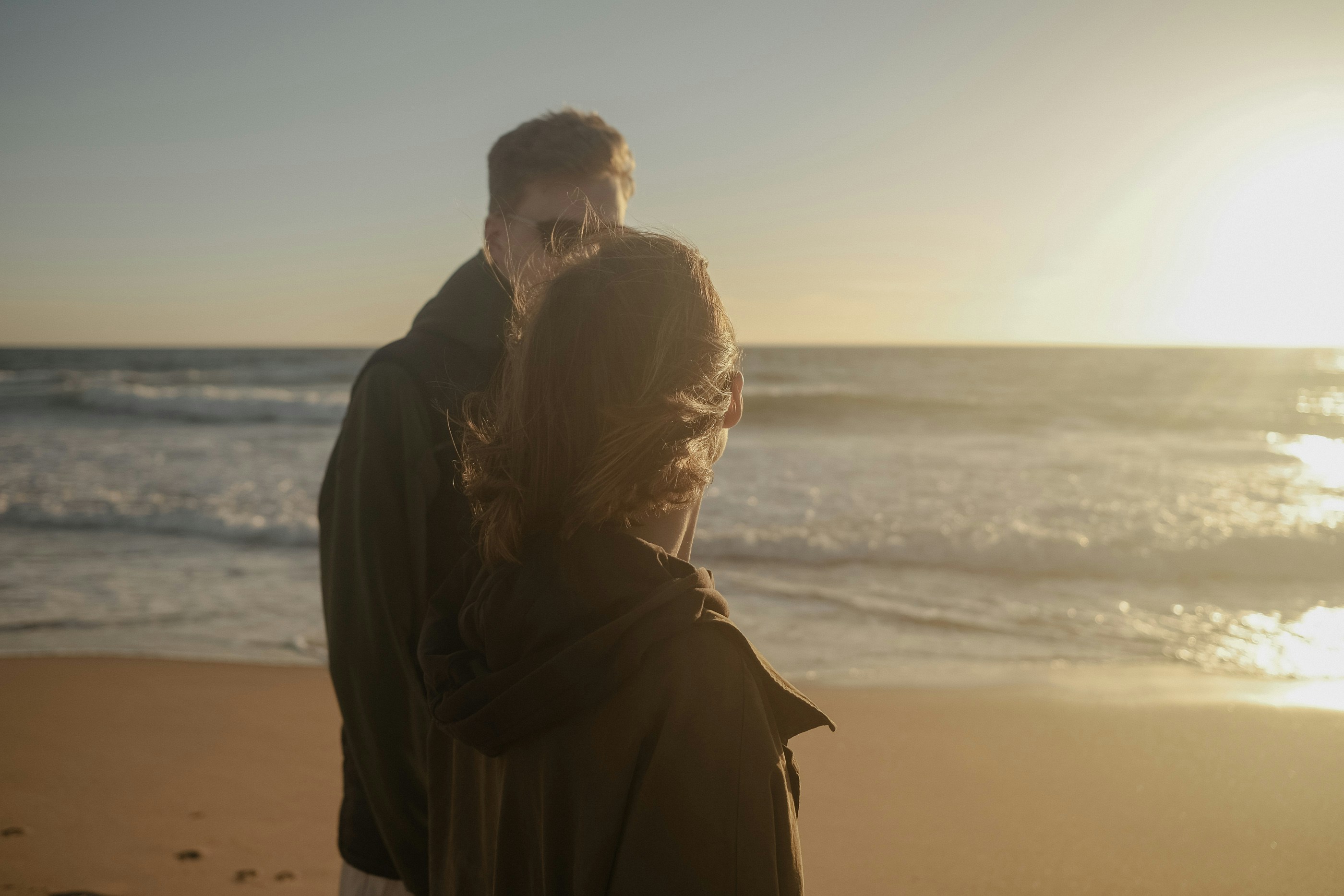 a man and woman standing on a beach next to the ocean
