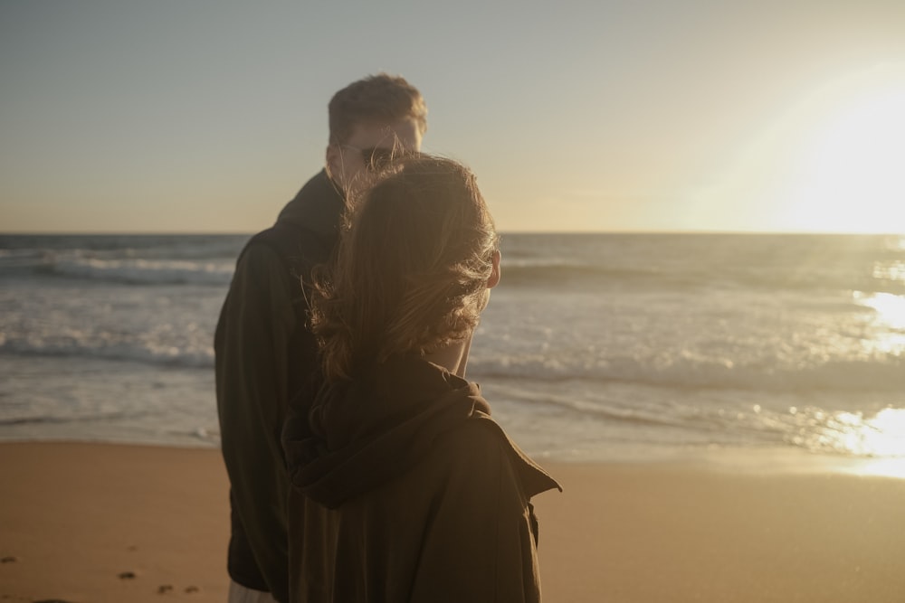 a man and woman standing on a beach next to the ocean