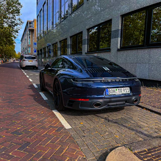 A sleek black Porsche parked in a modern urban setting at sunset.