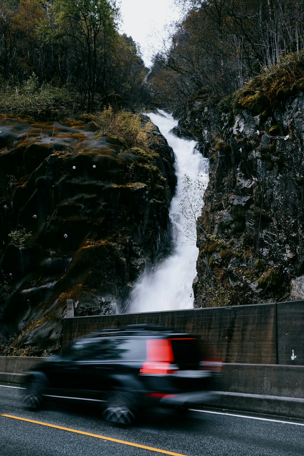 a car driving down a road near a waterfall
