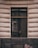 A window is set in a textured building facade with prominent horizontal grooves. The glass of the window shows reflections and appears slightly dirty or weathered. The frame of the window is dark, contrasting with the lighter color of the wall. Subtle reflections and possibly a hint of something inside can be seen on the window's surface.