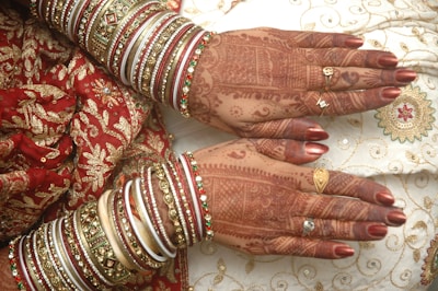 Intricate henna designs adorn the hands, complemented by elaborate bangles in various colors and intricate patterns. The attire features exquisite embroidery with golden and red motifs, highlighting a traditional and festive aesthetic.