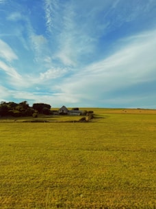Spacious countryside home surrounded by green fields under a bright blue sky.