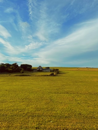 Spacious countryside home surrounded by green fields under a bright blue sky.