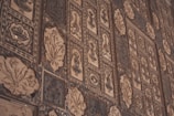Intricate wall tiles featuring various ornamental patterns and designs, including floral motifs and geometric shapes, in a mix of dark and light brown hues.