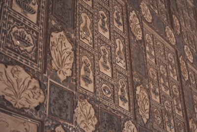 Intricate wall tiles featuring various ornamental patterns and designs, including floral motifs and geometric shapes, in a mix of dark and light brown hues.