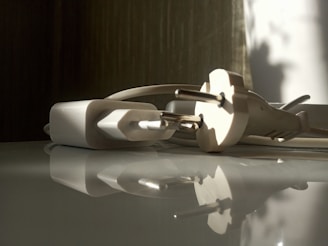 A close-up view of a white electrical plug and adapter lying on a reflective surface. Soft shadows and natural light illuminate the scene, creating a tranquil and calm atmosphere.
