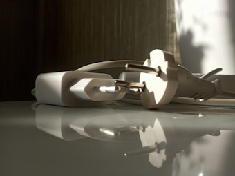 A close-up view of a white electrical plug and adapter lying on a reflective surface. Soft shadows and natural light illuminate the scene, creating a tranquil and calm atmosphere.