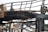 A close-up view of a charred metal structure. The metal beams and framework seem to have been severely damaged by fire. The surface of the metal is blackened and covered with soot, and parts of the structure appear to be twisted and melted.