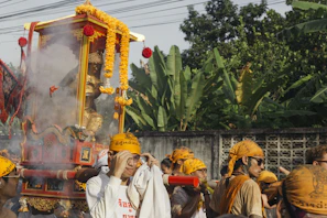 A vibrant procession of devotees carrying religious icons through a sunlit street.