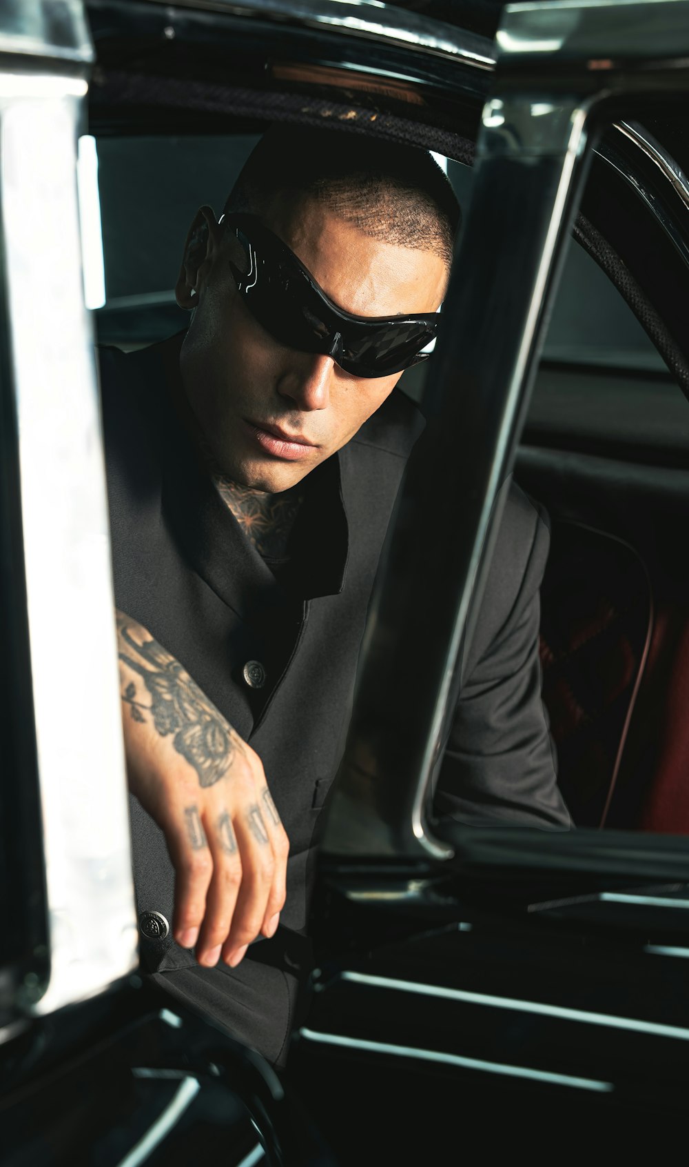 a man in a black shirt and sunglasses sitting in a car