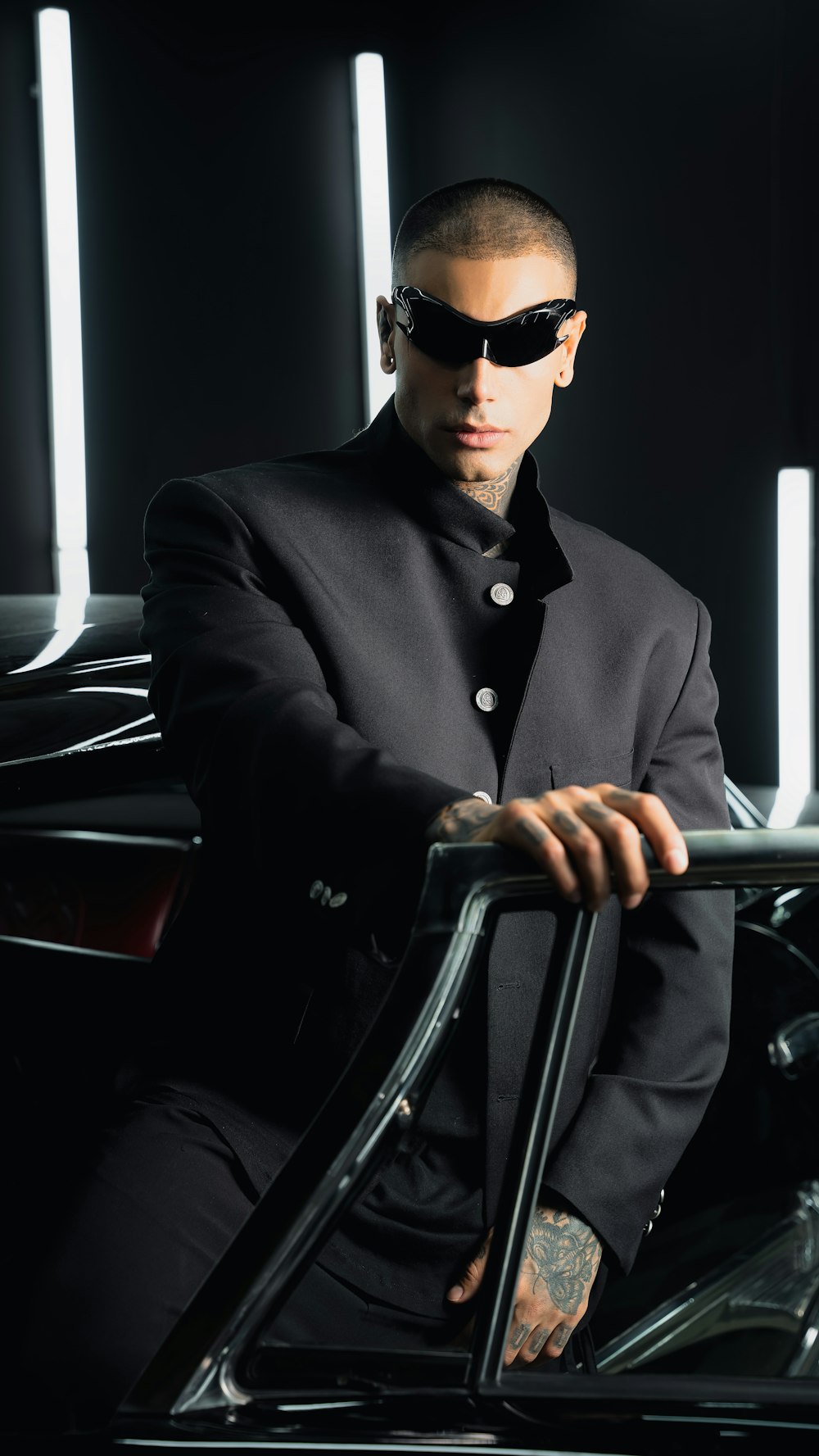 a man in a suit and sunglasses leaning on a car