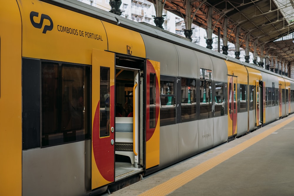 Un train jaune et gris est garé jusqu’à la gare
