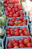 Close-up of ripe tomatoes and leafy greens arranged neatly in baskets.