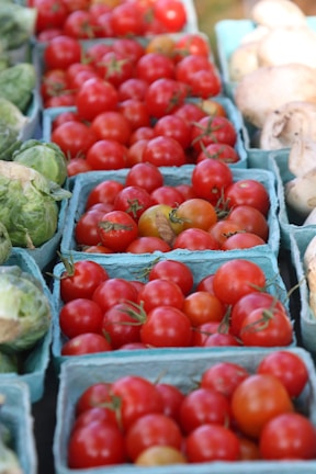 Close-up of ripe tomatoes and leafy greens arranged neatly in baskets.