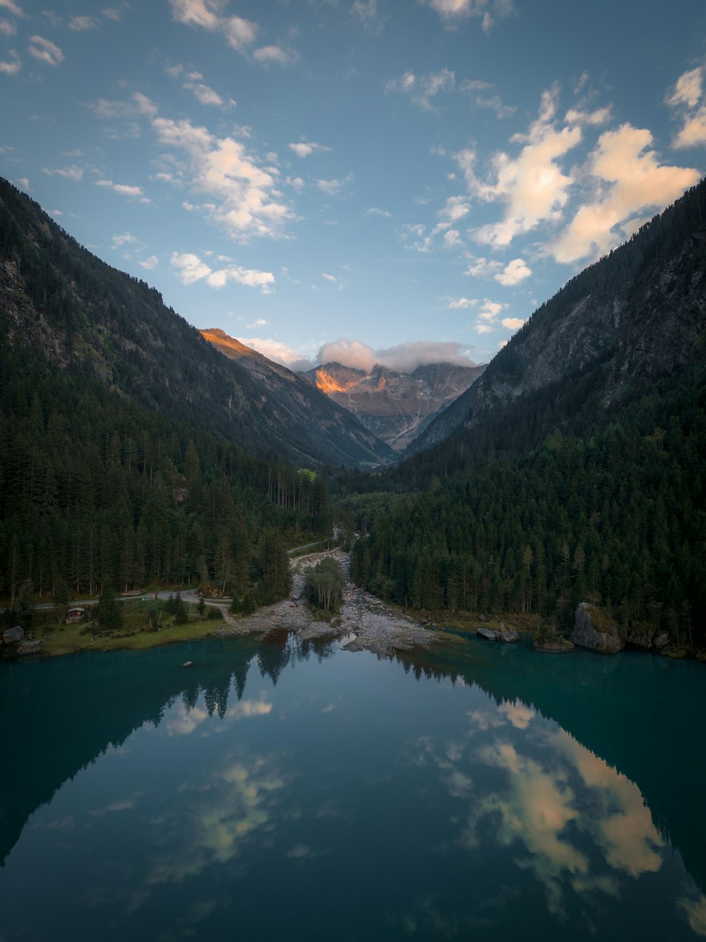 a lake surrounded by mountains and trees under a cloudy sky