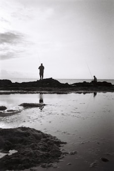 Two friends smiling and holding fishing rods together by a peaceful lake at sunrise.