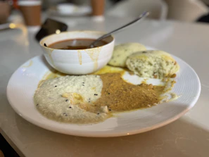 A steaming cup of masala chai next to a plate of baked moong dal chilla with fresh tomato salsa