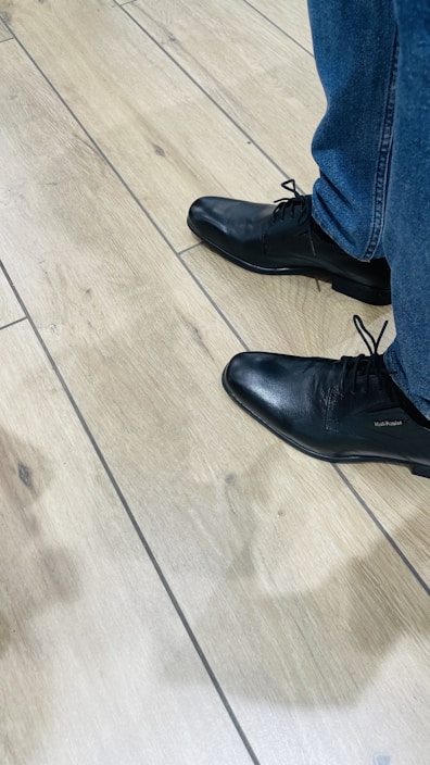 A pair of sleek black leather shoes on a wooden floor.