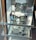 A display shelf with three pairs of sunglasses is positioned on mirrored surfaces, reflecting their image below. The sunglasses feature brown tortoiseshell frames with green-tinted lenses. The shelves are placed in a well-lit area, possibly near a window, contributing to reflections and a sleek presentation.