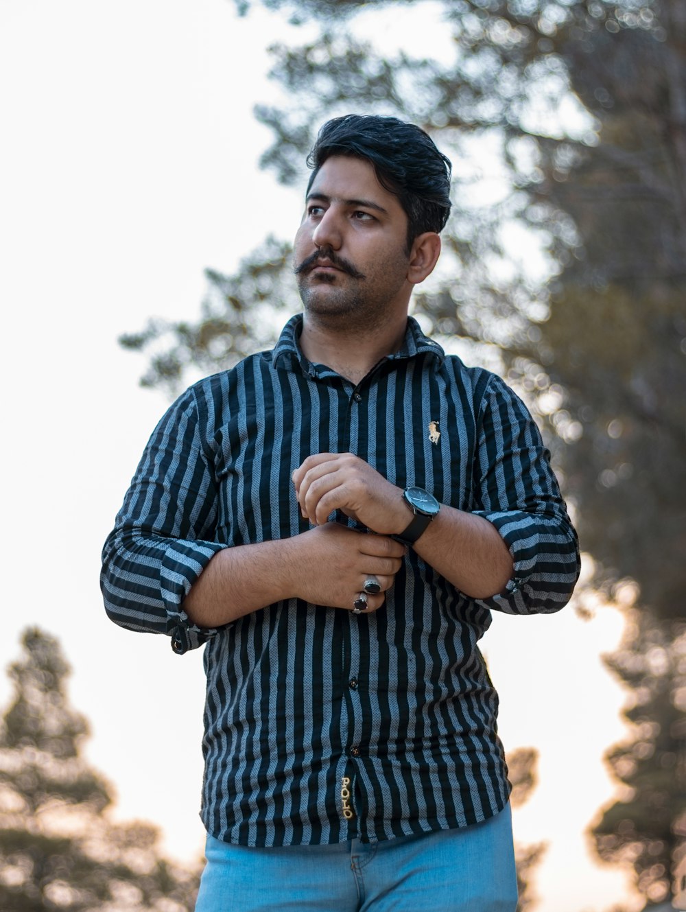 a man standing with his arms crossed in front of trees