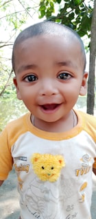 A smiling child holding a colorful cute mudy backpack outdoors on a sunny day