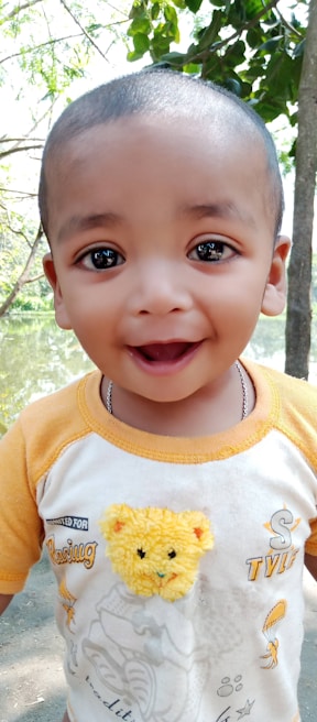 A smiling child holding a colorful cute mudy backpack outdoors on a sunny day