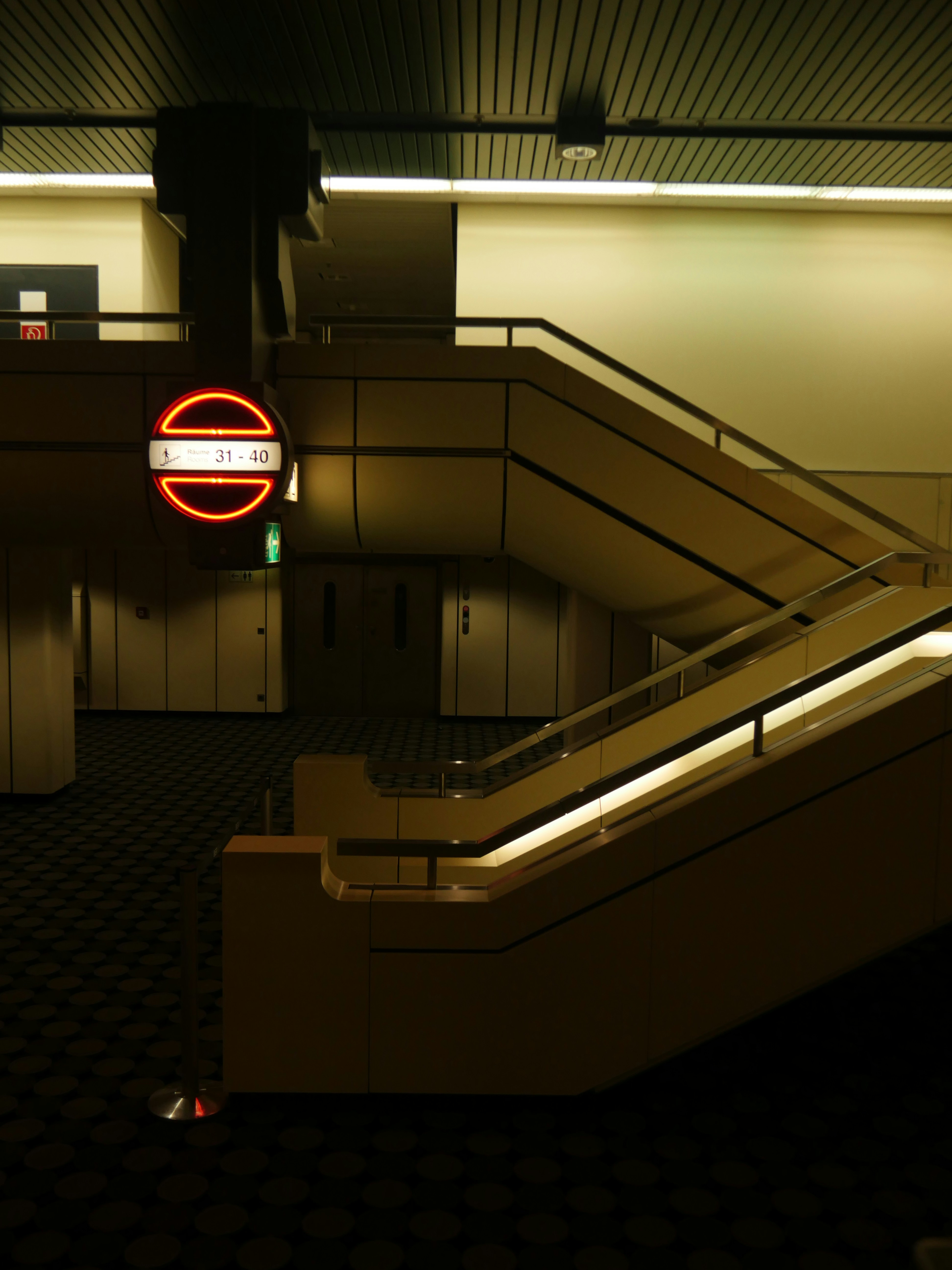 an escalator in a building with a neon sign above it