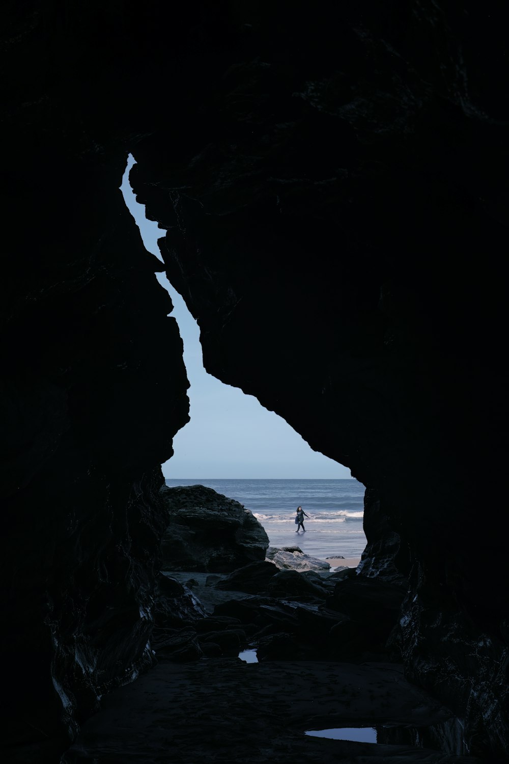 eine Person, die in einer Höhle steht und auf den Ozean blickt