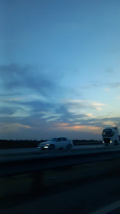 A chaplain praying with a truck driver beside a big rig on a quiet highway at sunset.