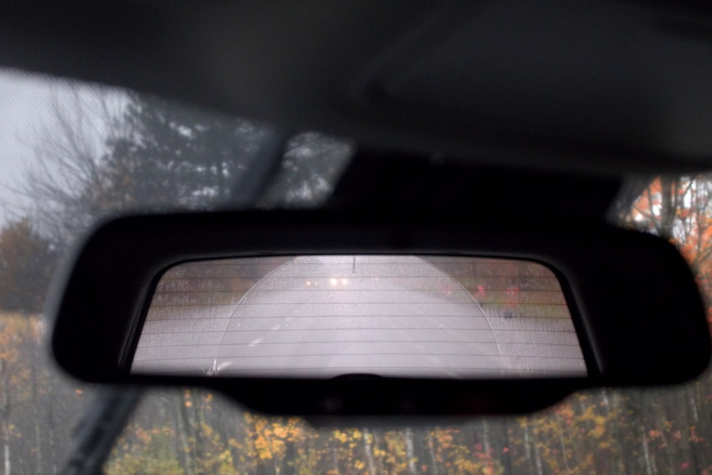 a rear view mirror of a car with trees in the background
